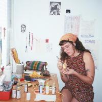 Milena sentada trabajando con diversos materiales sobre un escritorio.